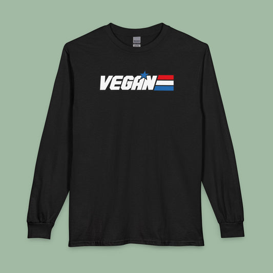A black long-sleeve t-shirt with a 'VEGAN' graphic on the chest, featuring a white text logo and a small blue star above a red, white, and blue striped flag, displayed on a solid sage green background.
