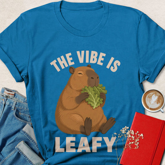 Teal-blue graphic t-shirt with capybara and leafy greens, text 'THE VIBE IS LEAFY'