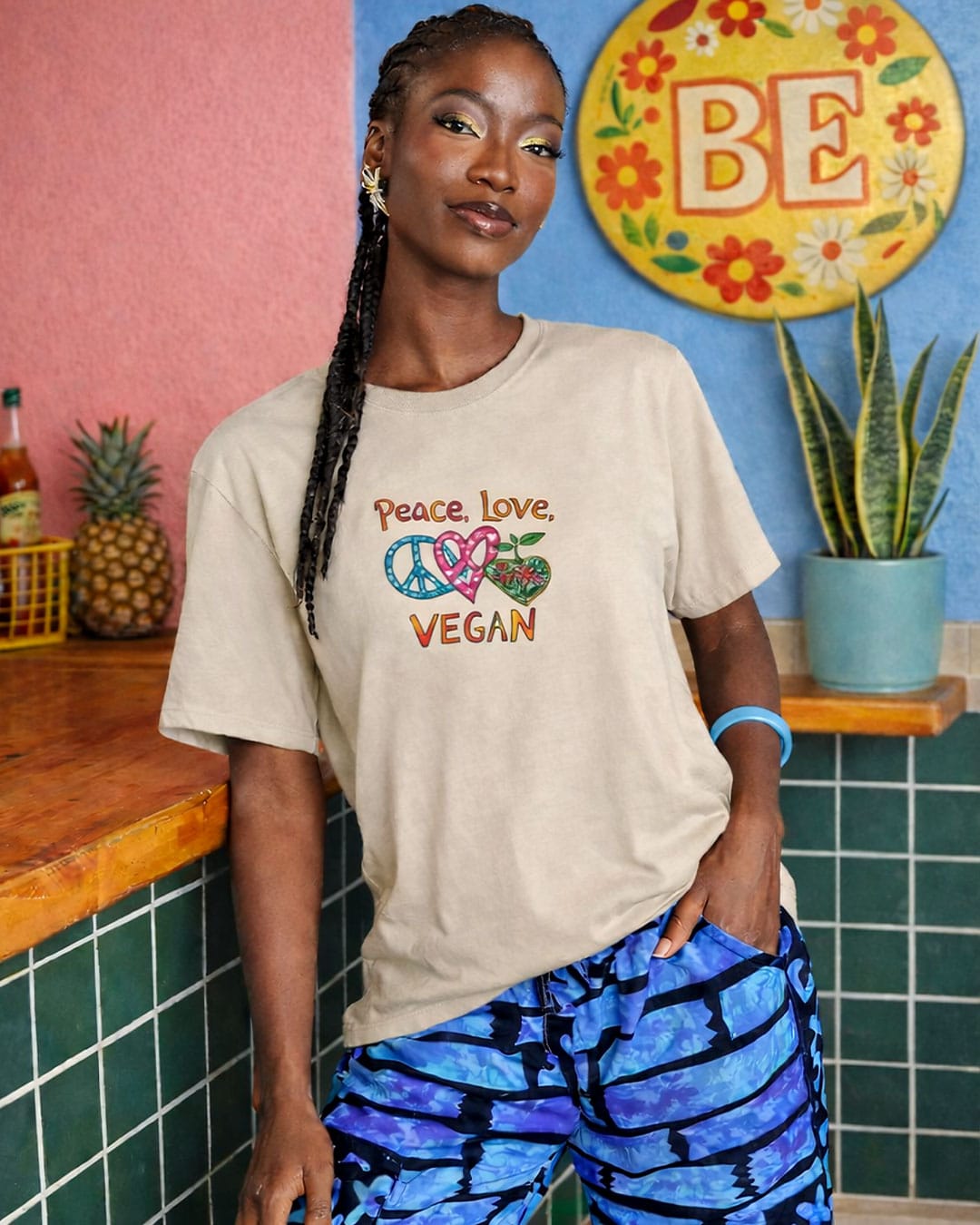 Person wearing a 'Peace Love Vegan' t-shirt in a colorful room.