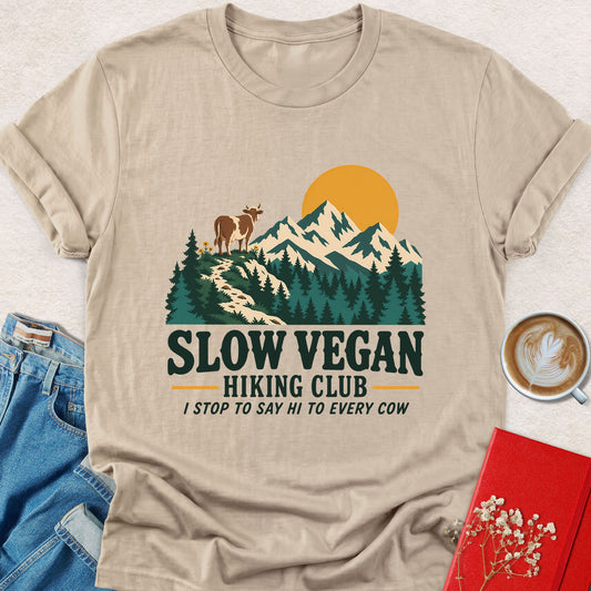 Sand-colored t-shirt with outdoor mountain and animal graphic and “Slow Vegan Hiking Club” text