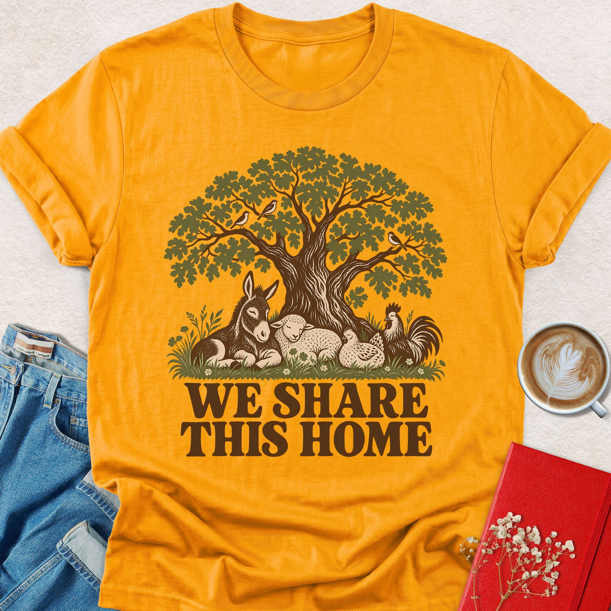 Gold crewneck T-shirt with tree-and-animals graphic and 'WE SHARE THIS HOME' text